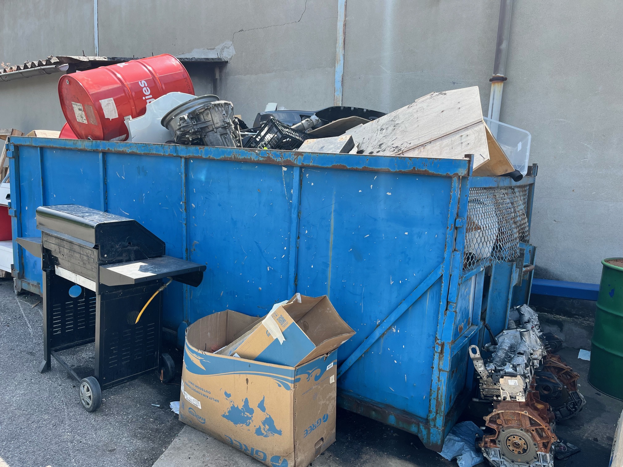 Benne bleu pleine d'objets encombrants dedans et autour